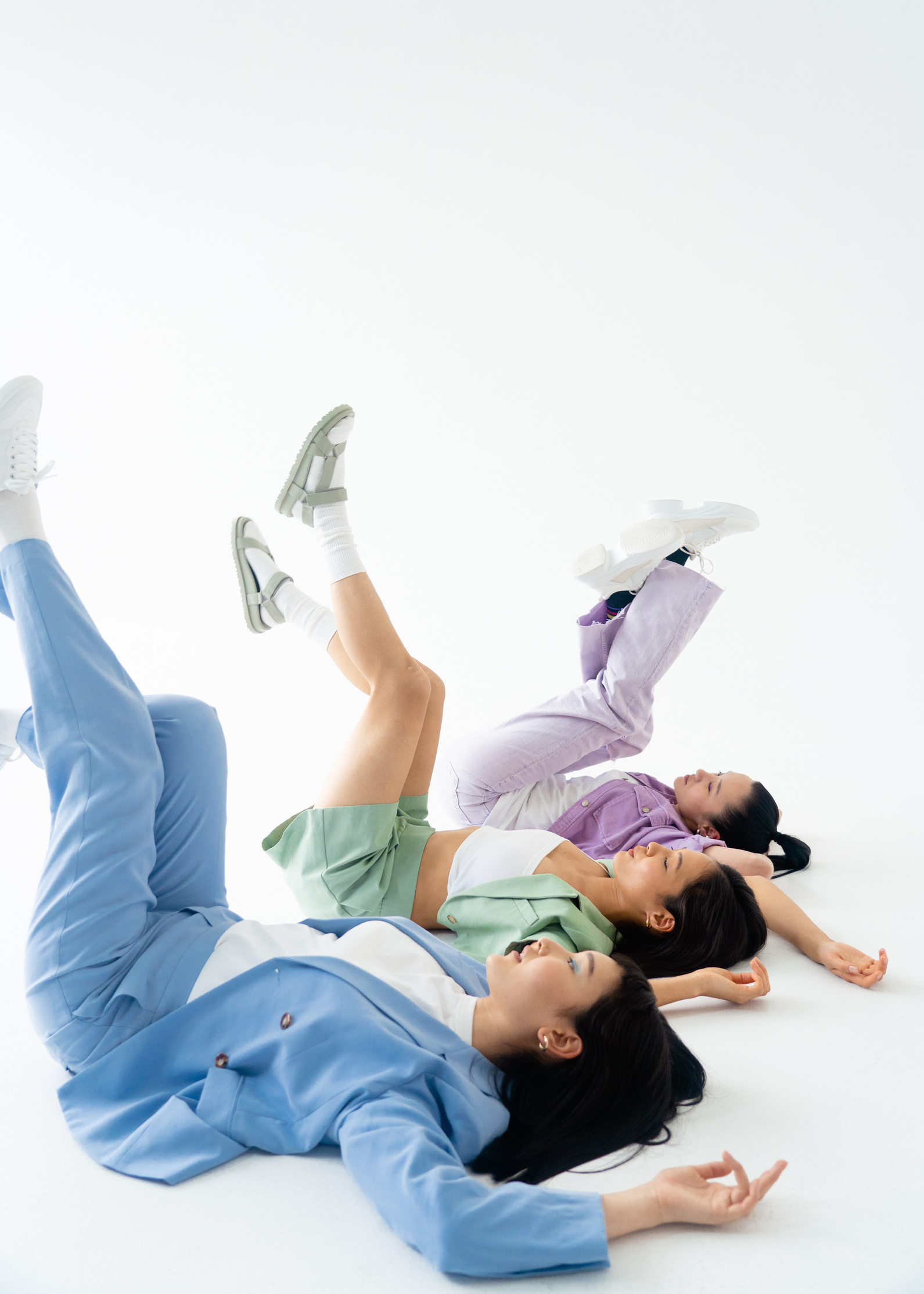 Women Wearing Pastel Color Outfit Lying on White Floor while Lifting their Legs
